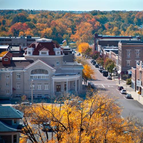 Aerial view of a town with autumn foliage, featuring buildings, streets, and colorful trees.