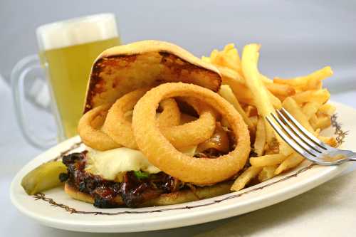 A hearty burger topped with onion rings, served with fries and a glass of beer in the background.