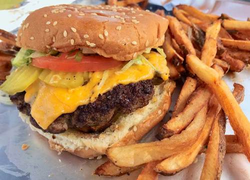 A juicy cheeseburger with lettuce, tomato, and pickles, served with a side of crispy French fries.