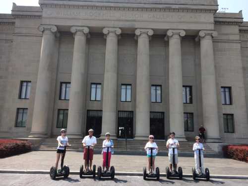 A group of six people on Segways in front of a large, classical-style art gallery building.