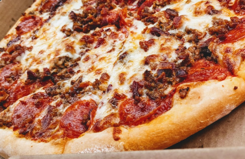 A close-up of a pepperoni and sausage pizza with melted cheese on a golden crust, in a pizza box.