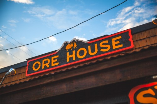 Sign for "Ore House" featuring mountains and wildlife, set against a blue sky with clouds.