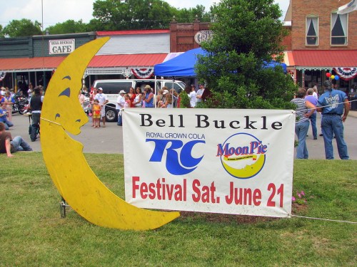 A large yellow crescent moon sign next to a banner for the Bell Buckle Festival featuring RC Cola and Moon Pie.