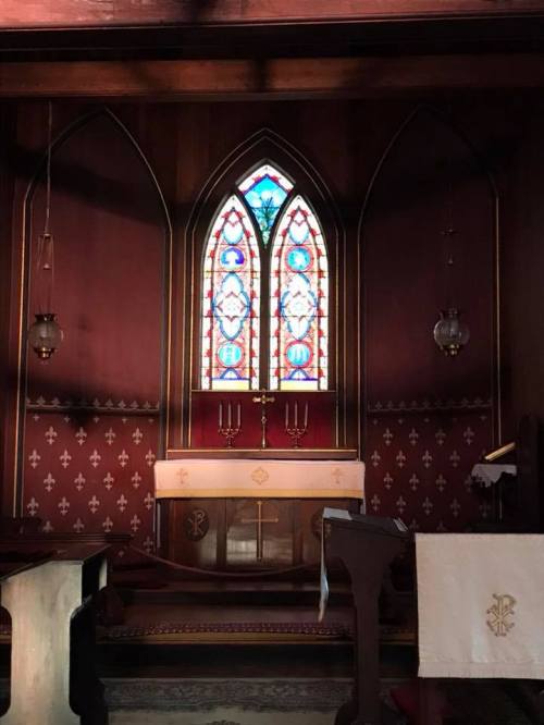 Interior of a church featuring a stained glass window, altar, and wooden pews with decorative patterns.