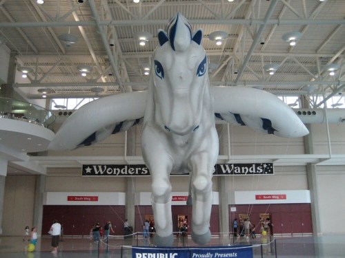 A large inflatable white unicorn with blue accents, suspended in a spacious indoor venue.