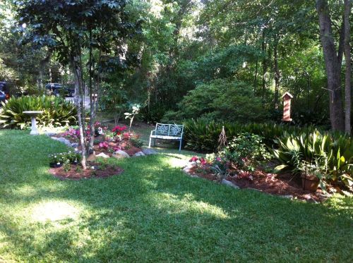 A serene garden scene featuring a green lawn, flower beds, a bench, and trees in a peaceful outdoor setting.