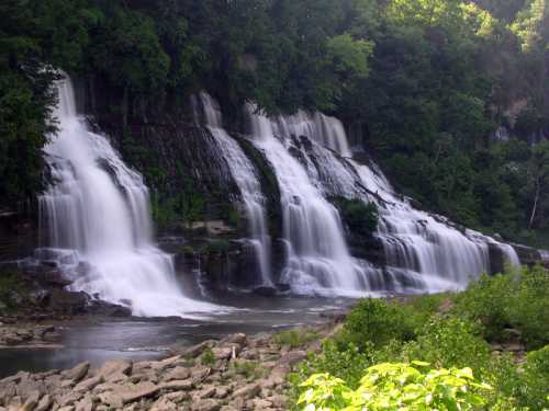 A serene waterfall cascading over rocky cliffs, surrounded by lush greenery and a calm river below.