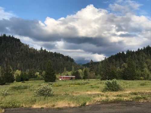 A red barn sits in a lush green field surrounded by mountains and cloudy skies.