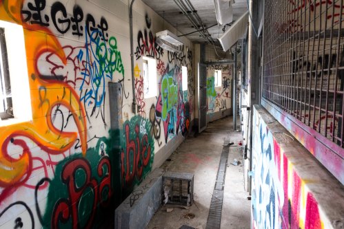 A dimly lit hallway with colorful graffiti on the walls and a metal grate along the floor.