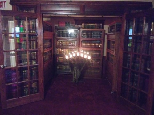 A cozy library with wooden shelves filled with books and a table of candles in the center, creating a warm atmosphere.
