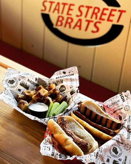 Two baskets of food: one with grilled sausages and the other with crispy potatoes, celery, and dipping sauce.
