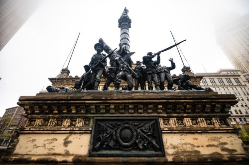 A bronze monument featuring soldiers in various poses, set against a foggy urban backdrop.
