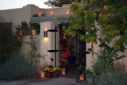 A warmly lit entrance with decorative lanterns, surrounded by plants and colorful pots, creating a welcoming atmosphere.