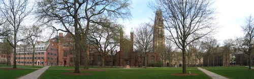 Panoramic view of a college campus featuring historic buildings, trees, and a tower under a cloudy sky.