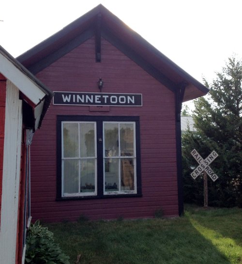 A purple building with a sign reading "Winnetoon" and a nearby railroad crossing sign. Green grass surrounds the area.