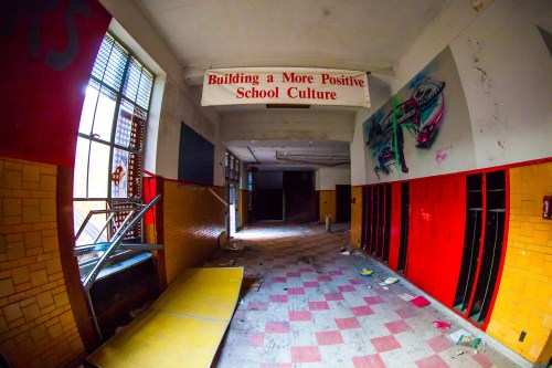 An empty, abandoned school hallway with red lockers and a banner reading "Building a More Positive School Culture."