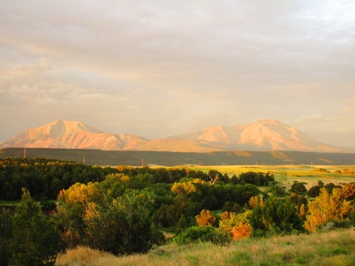Sunlit mountains rise above a lush green landscape under a cloudy sky, creating a serene natural scene.