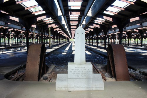 A monument honoring Central Railroad employees stands in an abandoned train station with rusted machinery and empty tracks.