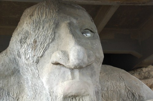 A close-up of a large, weathered concrete sculpture resembling a giant face with a prominent nose and textured features.