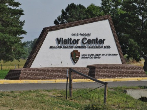 Sign for the Bighorn Canyon National Recreation Area Visitor Center, surrounded by trees and grass.