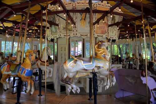 A colorful carousel with ornate horses and a vibrant canopy, surrounded by mirrors and decorative artwork.