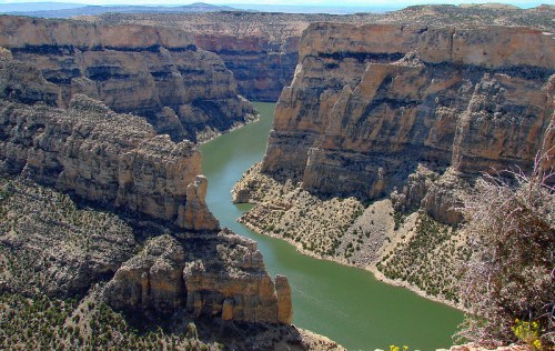 A scenic view of a winding river surrounded by steep, rocky cliffs and sparse vegetation under a clear blue sky.