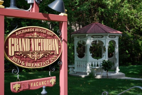 Sign for "Grand Victorian Bed & Breakfast Inn" with a gazebo in a lush green garden.