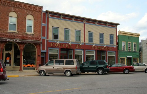 A street view of a small town featuring colorful buildings, including a coffee shop and parked cars.