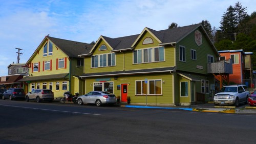 A colorful two-story building with a green exterior, featuring multiple windows and parked cars in front.