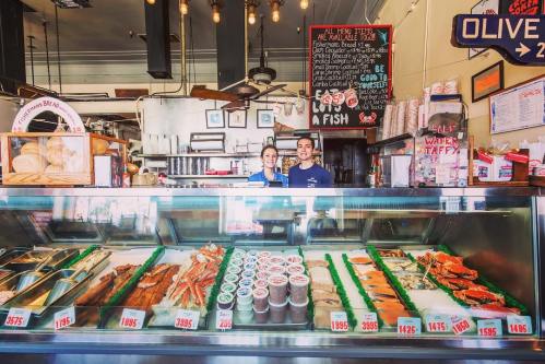 A seafood market display with fresh fish, seafood dishes, and two smiling employees behind the counter.