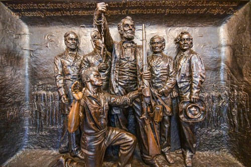 A bronze relief depicting historical figures, including a central figure holding chains, symbolizing justice and freedom.