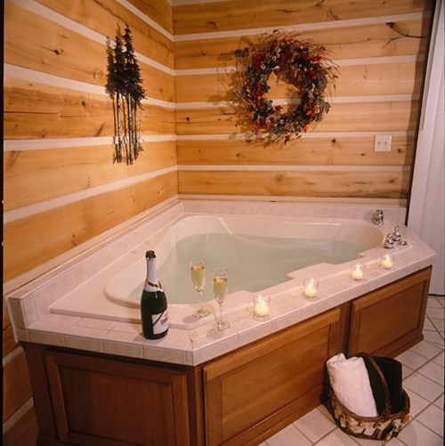 Cozy bathroom with a jetted tub, candles, champagne, and a decorative wreath on wooden walls.