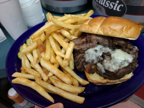 A plate with a roast beef sandwich topped with melted cheese, accompanied by a side of golden French fries.