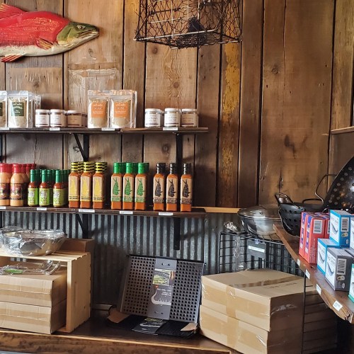 A rustic wooden shelf displays various jars, sauces, and kitchen items, with a fish decoration on the wall above.
