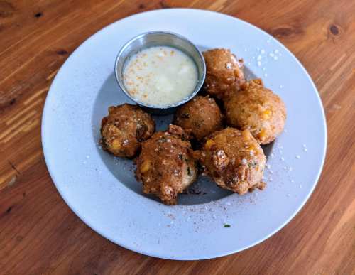 A plate of golden-brown fritters served with a small bowl of dipping sauce on a wooden table.