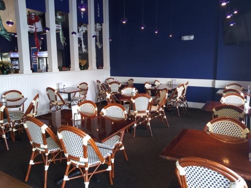 A spacious restaurant interior with wooden tables and wicker chairs, featuring blue walls and pendant lighting.