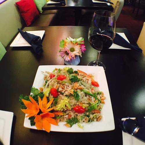 A colorful plate of salad with vegetables, nuts, and flowers, accompanied by a glass of red wine on a dining table.