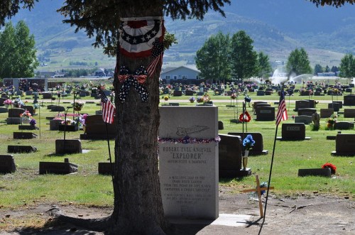 A cemetery with numerous gravestones, decorated with flags and flowers, featuring a memorial stone for Robert E. Knivila.