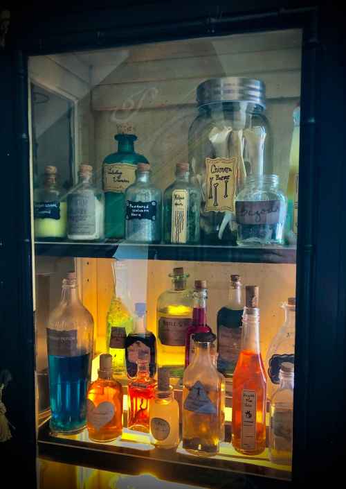 A display of colorful potion bottles and jars on shelves, labeled with various names and filled with vibrant liquids.