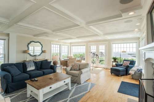 Bright, airy living room with blue sofas, a wooden coffee table, and large windows overlooking a scenic view.