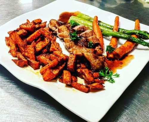 A plate of seasoned sweet potato fries, grilled chicken, and sautéed asparagus, garnished with parsley.