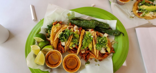 A vibrant plate of tacos topped with onions and cilantro, accompanied by lime wedges and two sauces.