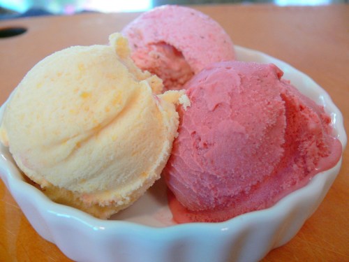 A small dish containing three scoops of ice cream: yellow, pink, and a light red.