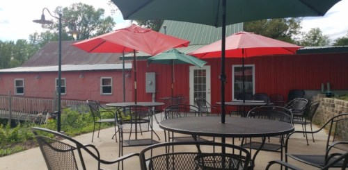 Outdoor seating area with black tables and colorful umbrellas in front of a red barn-style building.