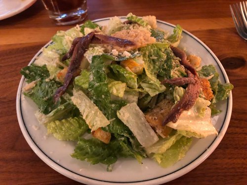 A fresh Caesar salad with romaine lettuce, croutons, anchovies, and grated cheese on a white plate.