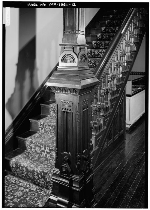 A detailed wooden staircase with ornate banister and patterned carpet, showcasing intricate craftsmanship.