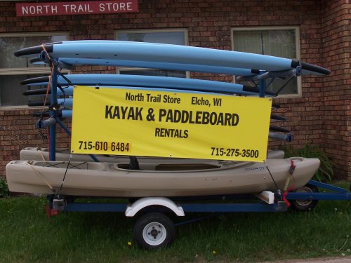 A trailer with kayaks and paddleboards, featuring a sign for rentals at North Trail Store in Elcho, WI.