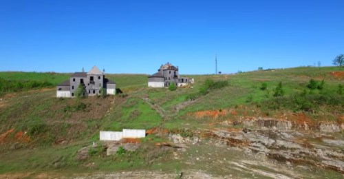 Abandoned buildings on a hillside with clear blue sky and green vegetation surrounding them.