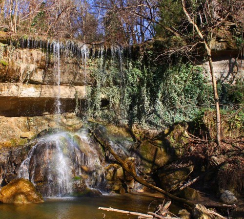 A serene waterfall cascading over rocky cliffs, surrounded by lush greenery and trees under a clear blue sky.