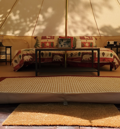 Cozy tent interior with a patterned bedspread, side tables, and a rug, creating a warm, inviting atmosphere.